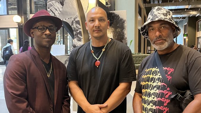 three Black men stand inside a large art exhibit and station in Oakland