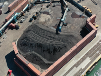 A drone aerial shot of large pile of dark dust, which is coal, inside an open top container