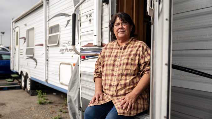 A woman sits on the front step of a trailer home