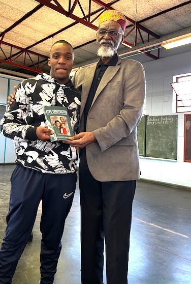 An elder African American man holds up a book with a young African man