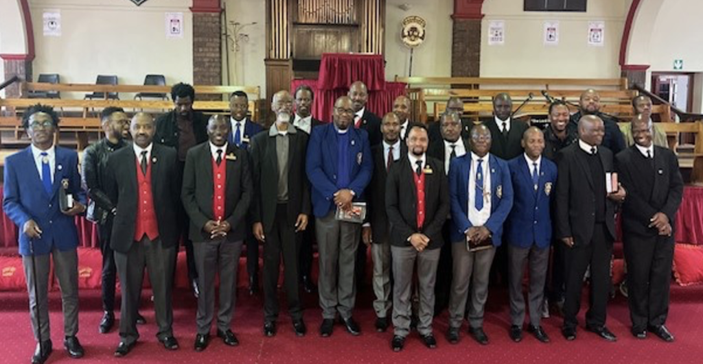 a group of mostly Black men in South Africa dressed in suits pose for a photo inside a church