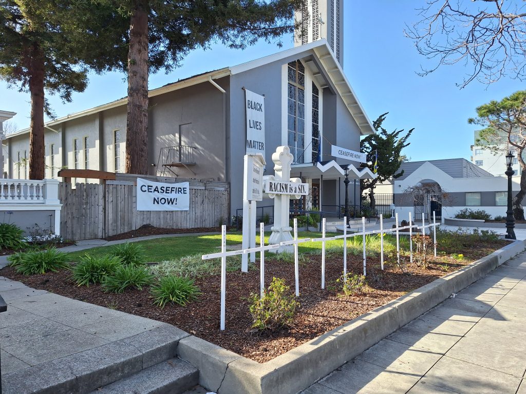 a small grey and white church building with signs on the front