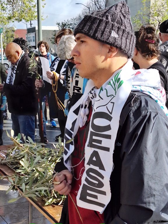 A young man wearing a beanie and white ceasefire scarf walks in a march